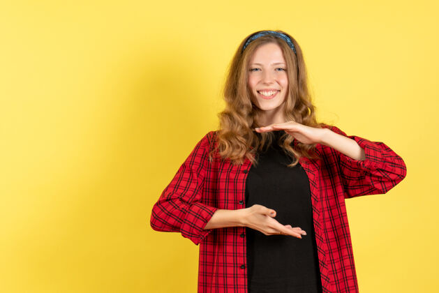 人正面图身着红色格子衬衫的年轻女性在黄色背景上摆姿势微笑女孩女性情感模特彩色人类年轻女性购物者格子