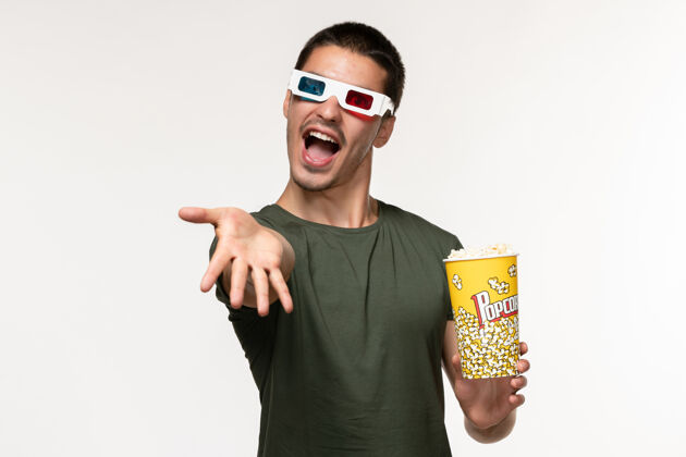 电影正面图身着绿色t恤的年轻男性手持爆米花包戴着d墨镜在白墙上拍摄电影《孤独的电影院》男性男人包装爆米花