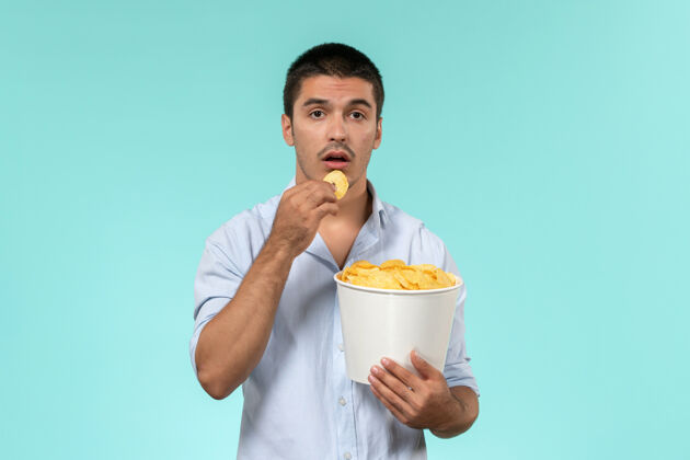 电影前视图年轻人拿着篮子和土豆cips在一个蓝色的墙上电影远程电影院电影早餐杯子