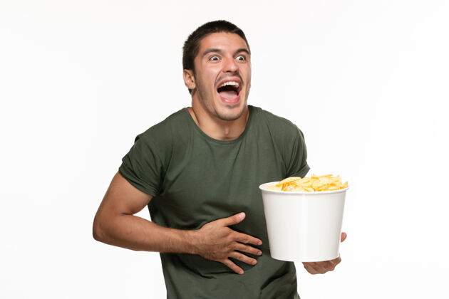 观看正面图身穿绿色t恤的年轻男子拿着篮子和土豆在看电影在白墙上孤独的电影早餐电影电影