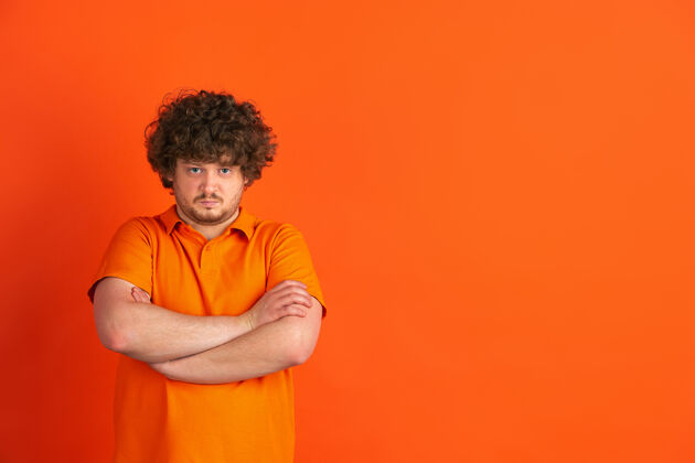 手势严肃的双手交叉着橙色工作室里白人年轻人的单色肖像广告专业成功