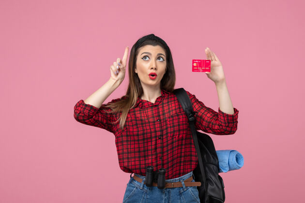 银行正面图身穿红色衬衫的年轻女性手持粉色背景的银行卡人类女性颜色脸年轻的女性人