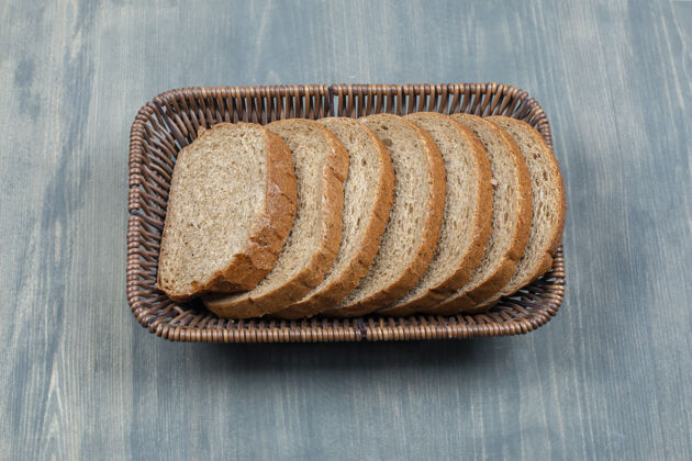 面包屑石桌上放着柳条筐的黑面包片食品早餐切片