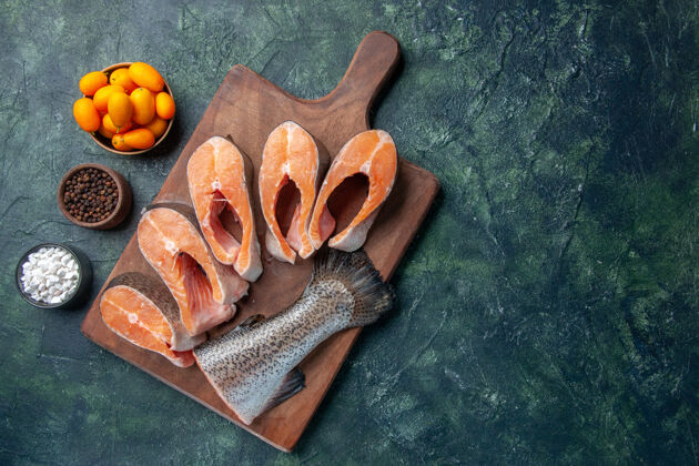 金橘木砧板上的新鲜生鱼和深色混搭桌上的金橘辣椒的俯视图混合食物深色