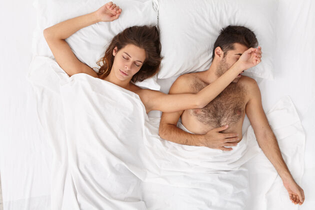 蜜月放松的女人俯视图舒展双手与丈夫睡觉 在舒适的卧室白色床上摆姿势 男人感到不舒服夫妻一起休息 深度睡眠睡觉时间 休息理念男朋友丈夫懒惰