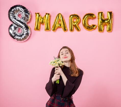 妇女节正面图：手拿鲜花的年轻女性 粉色背景上的三月装饰 呈现妇女节三月激情派对平等感性年轻的女性8花