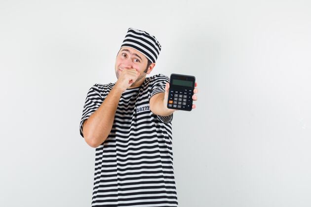 休闲年轻的男性穿着t恤 戴着帽子 面带羞耻的样子展示计算器正面图男人人帽子