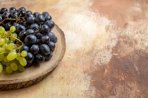 健康侧面特写镜头：一串串的黑葡萄和绿葡萄放在砧板上水果浆果束