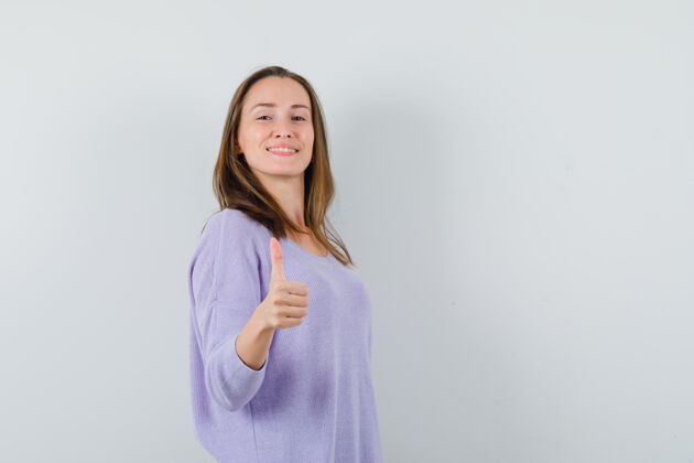 卷曲身穿淡紫色上衣的年轻女子竖起大拇指 看上去很高兴衬衫姿势自信