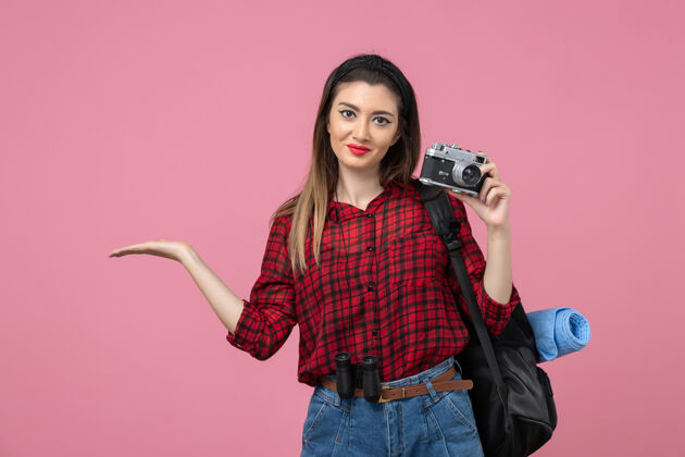 相机前视图年轻女性正在用相机拍摄粉红色背景的女性照片模型头发肖像黑发