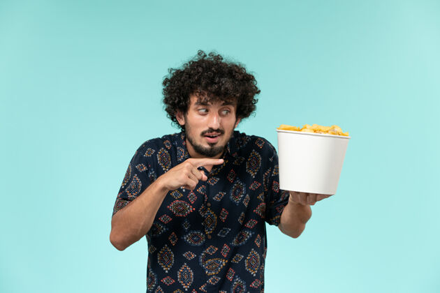 肖像前视图年轻人拿着篮子和土豆cips在一个蓝色的墙上遥远的电影院电影电影电影