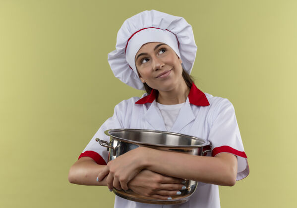空间穿着厨师制服的年轻快乐的白人厨师女孩手拿着锅 看着绿色的一面 留着复制的空间女孩复制制服