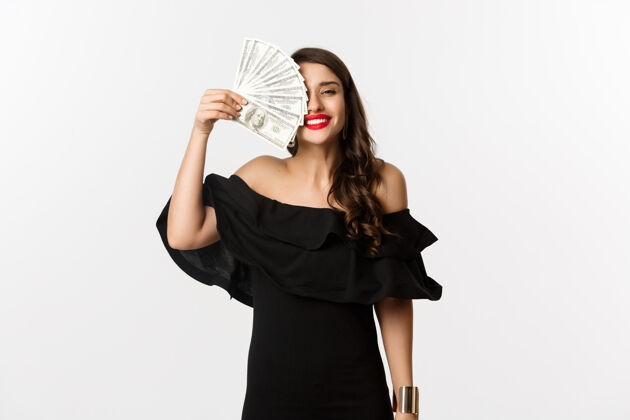 表情时尚和购物理念快乐的年轻女子穿着黑色连衣裙 红唇 抱着钱 微笑着满意 站在白色的背景上优雅魅力年轻