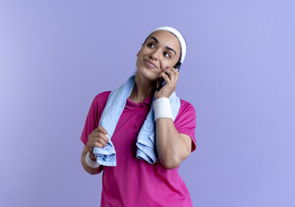 运动年轻快乐的白人运动女性戴着头带和腕带拿着毛巾围着脖子在紫色的手机上聊天 还有复印空间持有毛巾头带