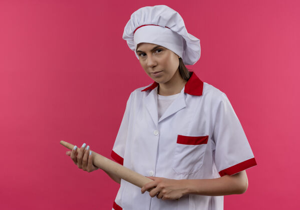 信心穿着厨师制服的年轻自信的白人厨师女孩手持擀面杖 看着粉色的相机 还有复印空间卷厨师烹饪