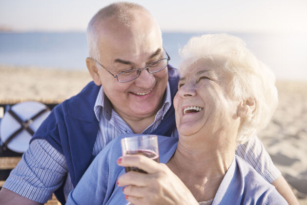 笑老两口在沙滩上拥抱喝红酒享受婚礼快乐