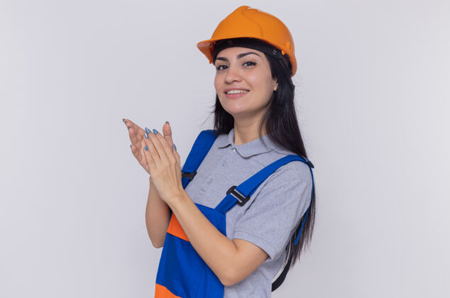 建筑身穿施工制服 头戴安全帽的年轻建筑工人站在白色的墙壁上 微笑着自信地鼓掌站立女人年轻