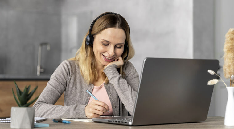 耳机戴着耳机在笔记本电脑上工作的女人设备技术学生