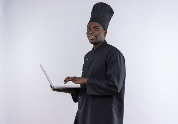 笔记本电脑身着厨师制服的年轻美籍黑人厨师拿着笔记本电脑 看着白色的相机和复印空间持有副本非裔美国人