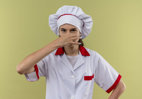 手穿着厨师制服的年轻恼怒的白人厨师女孩用手捂住鼻子放在绿色的地方厨师关闭年轻