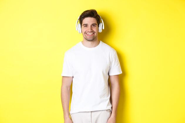 男人年轻帅哥戴着耳机听音乐 戴着耳机微笑着 站在黄色的背景上年轻男人自信