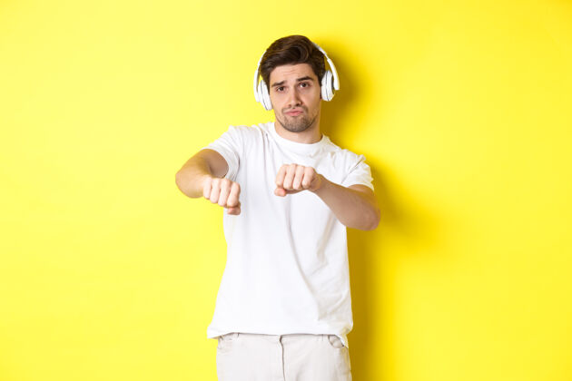 演播室很酷的家伙戴着耳机听音乐跳舞 穿着白衣服站在黄色的工作室背景下帅哥表情耳机