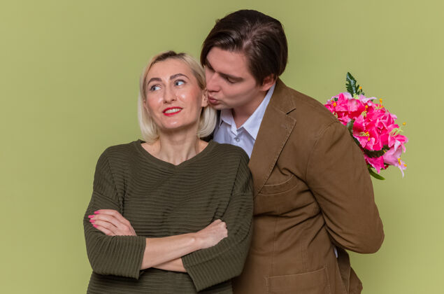 吻年轻漂亮的情侣背着花束的快乐男人站在绿色的墙上亲吻他可爱的女友庆祝国际妇女节花庆祝男人