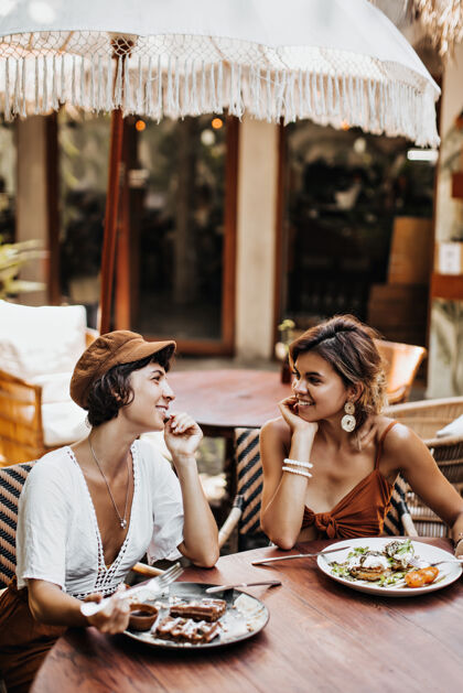 手掌两个穿着夏天时髦服装的女人在街边咖啡馆聊天 吃着美味的食物夏天皮肤友谊