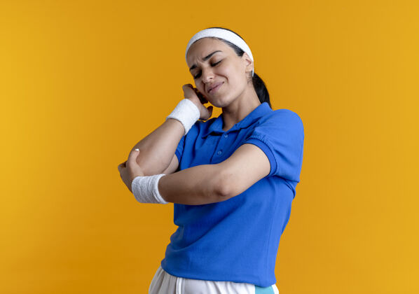 年轻年轻疼痛的高加索运动女性戴着头带和腕带手肘在橙色与复制空间肘部腕带复制