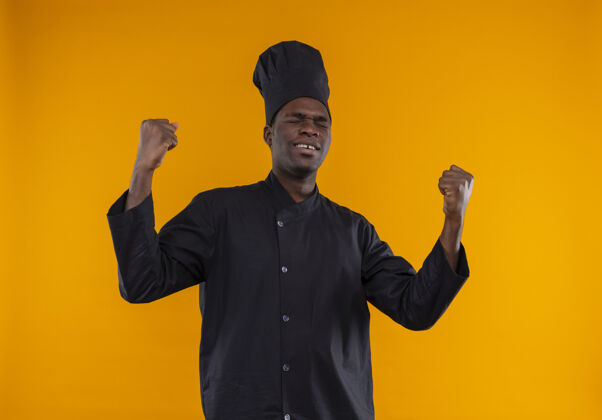 起来年轻的美籍黑人厨师身着厨师制服 闭上眼睛举起拳头 在橘子上留影眼睛厨师太空