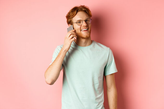 电话一个留着红头发和胡须的帅哥站在粉色背景下 一边打电话 一边开心地看着别人胡须姜沟通