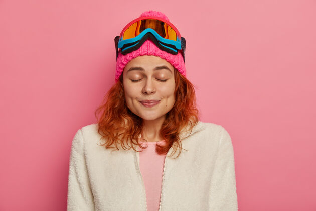 溜冰满意的红发女人戴着暖和的帽子 滑雪镜和白色套头衫套头衫女人魅力