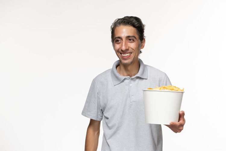 抱着正面图年轻的男性在吃薯片 在白色的表面微笑年轻的男人杯子电影院