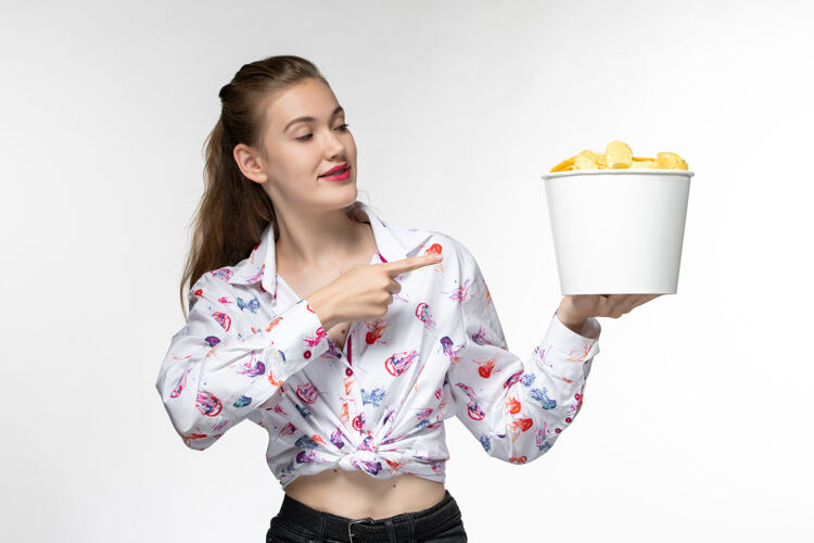 漂亮正面图：年轻的女性拿着土豆片篮子 微笑着站在白色的表面上专业电影土豆