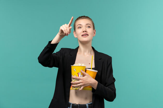 年轻女性正面图：年轻女子拿着爆米花喝酒 在蓝色的水面上看电影女商人剧院看