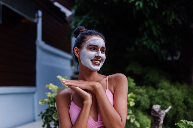 健康晒黑皮肤的户外写真美丽的高加索女子穿着比基尼在温泉浴场与白色脱皮面具在脸上自然旅行面膜