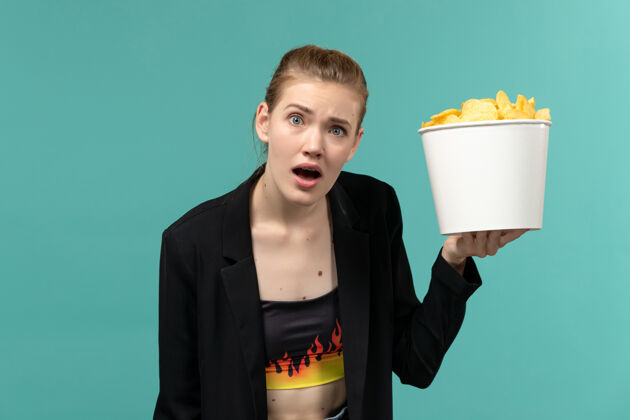 前面正面图：年轻的女性拿着薯片在蓝色的水面上看电影土豆年轻的女性杯子