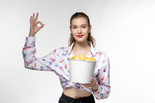 电影正面图：年轻的女性拿着土豆片篮子 微笑着站在白色的表面上前面漂亮土豆
