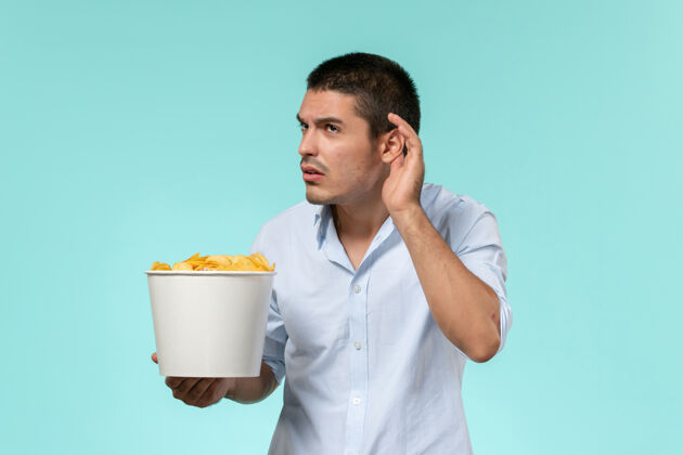 电影院前视图年轻的男性拿着篮子和薯片 试图听到一个蓝色的表面尝试电影远程