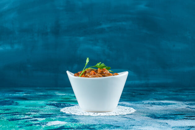 欧芹一碗烤豆放在杯垫上 蓝色背景美味豆子碗