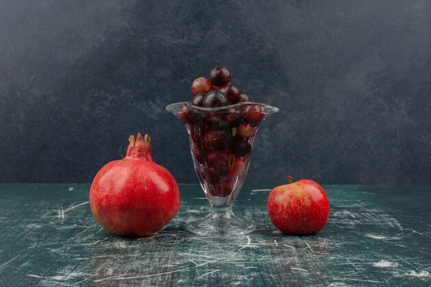 葡萄苹果 石榴和一杯黑葡萄放在大理石桌上成熟天然苹果