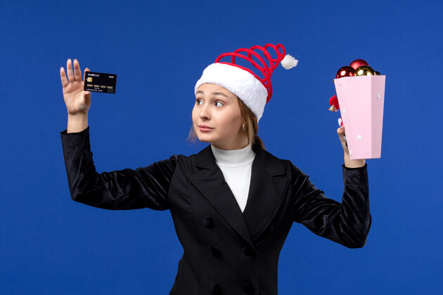 举行前视图年轻女士拿着银行卡在蓝色墙上新年情感假期玩具微笑人圣诞节