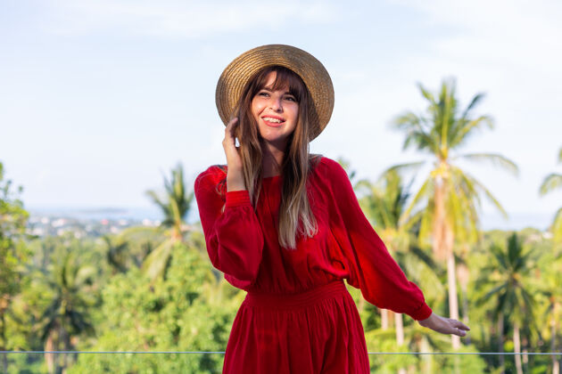 露台穿着红色夏装 戴着草帽 在阳台上享受热带海景和棕榈树的快乐女人女士夏季帽子