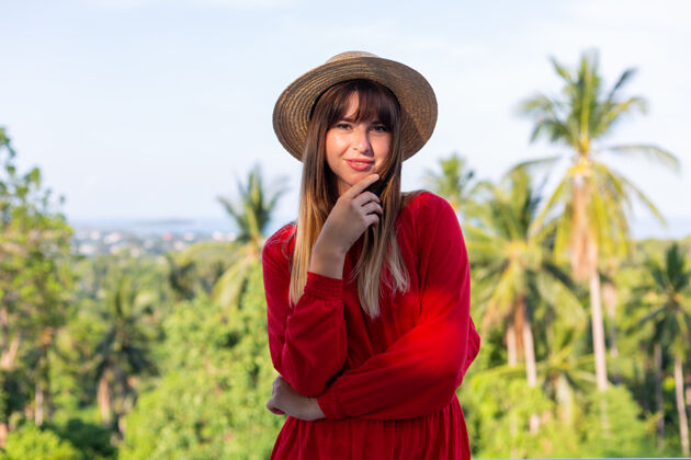 露台穿着红色夏装 戴着草帽 在阳台上享受热带海景和棕榈树的快乐女人女士红色优雅