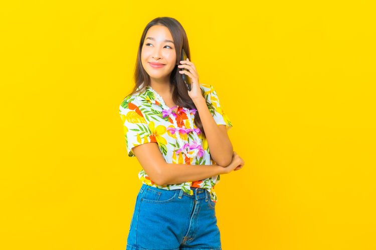 美丽美丽的亚洲年轻女子穿着彩色衬衫在黄色墙上用智能手机拍照女人眼镜假日