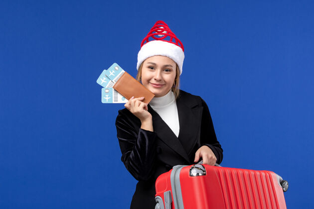 人正面图年轻女性手持包和机票在蓝墙飞机度假之旅女人前面商人