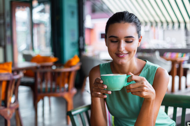 餐桌可爱 优雅 平静 快乐的女士 穿着绿色夏装 坐在咖啡馆里喝咖啡 享受早晨女士咖啡情绪