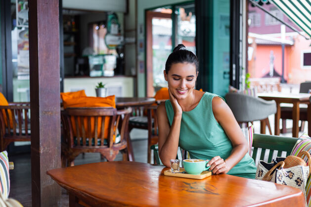 举行可爱 优雅 平静 快乐的女士 穿着绿色夏装 坐在咖啡馆里喝咖啡 享受早晨餐厅杯子优雅