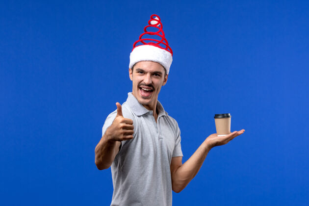 杯子正面图年轻男性手持塑料咖啡杯在蓝色办公桌上度假男性新年肖像人圣诞节