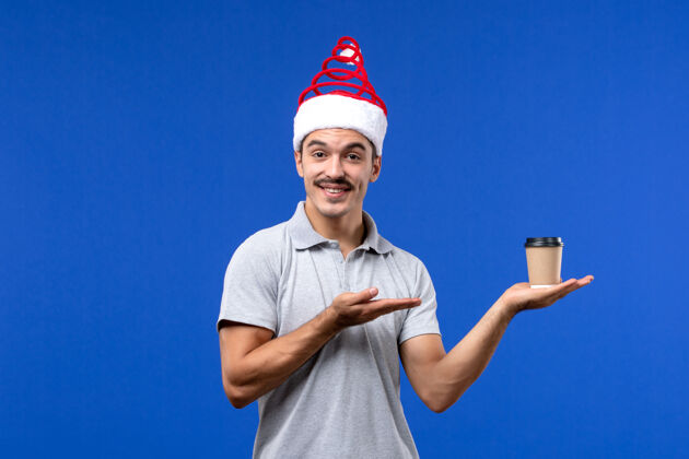 风景正面图年轻男子手持塑料咖啡杯在蓝色墙壁上度假男子新年咖啡快乐人